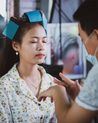 female hairdresser standing, face makeup and making hairstyle to cute lovely young woman in beauty salon